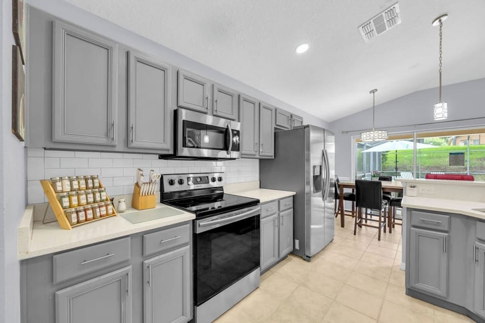 Modern kitchen w/ gray cabinetry, stainless steel appliances & a bright dining area nearby.