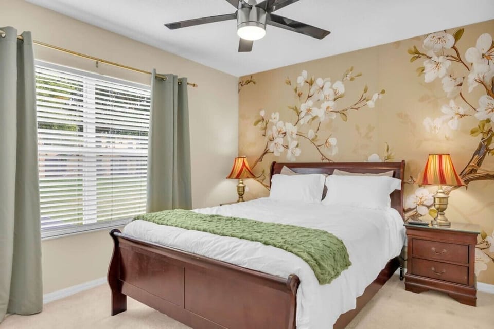 Classic bedroom w/ floral wallpaper, green bedding & warm lamp lighting for a cozy feel.