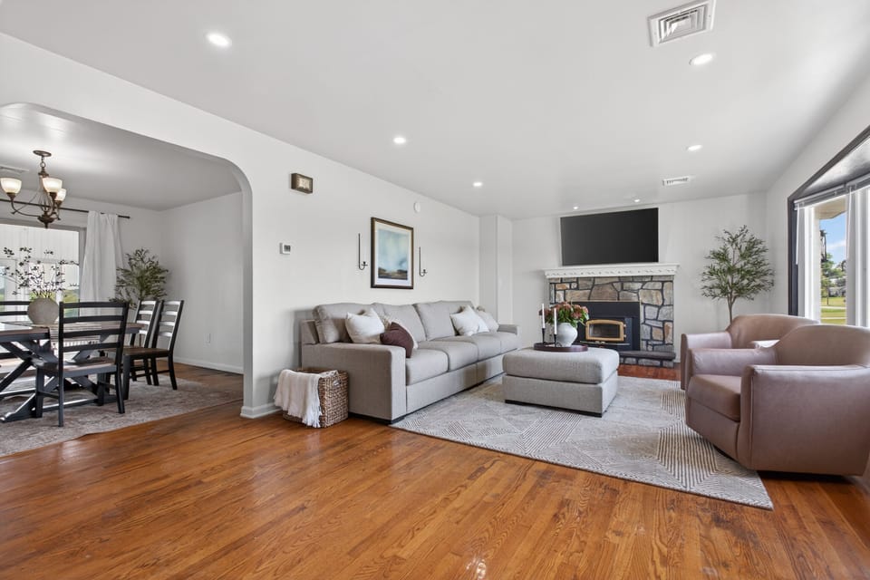 Bright open living room with stone fireplace, TV, and adjacent dining area
