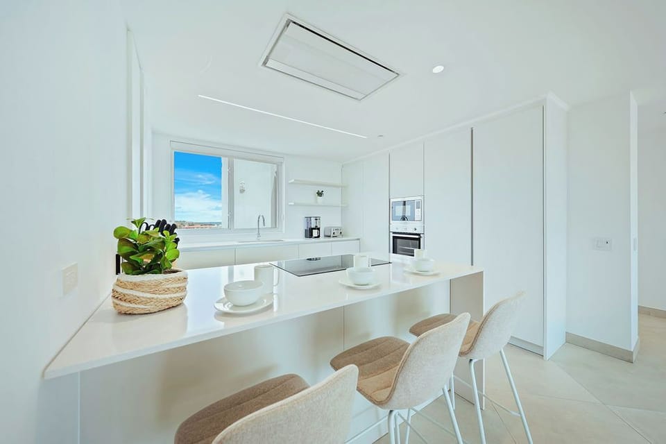 Your bright, modern kitchen offers sleek white cabinetry, built-in appliances, and a spacious breakfast bar overlooking sparkling sea views—perfect for morning coffee or casual dining.