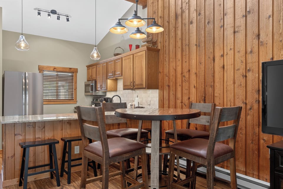 Your modern mountain retreat features a fully-equipped kitchen with stainless appliances, custom cabinetry, and a warm wood-paneled dining nook where you'll share meals and memories around the handcrafted table.
