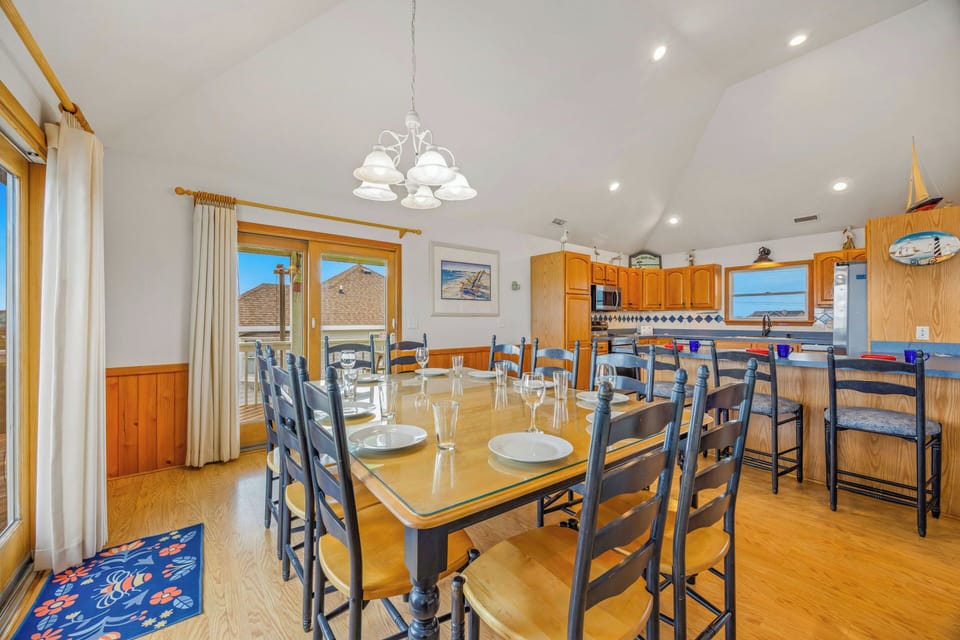 Gather around this inviting dining table for meals with your group, where coastal charm meets comfort. Large windows frame ocean views while the open kitchen keeps conversation flowing.