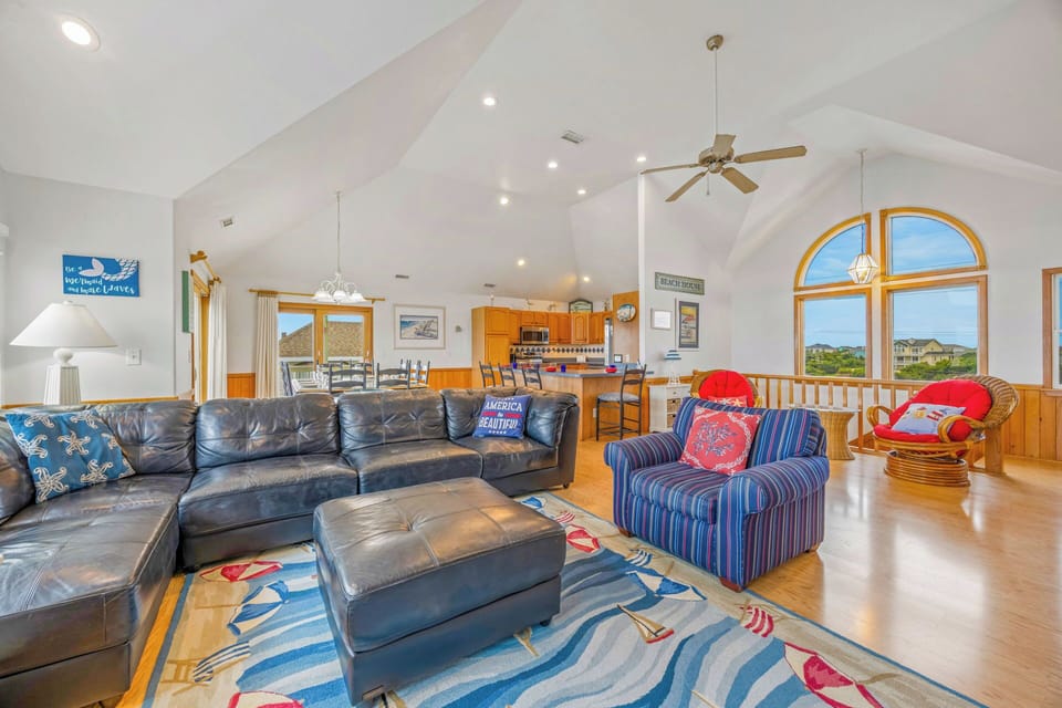 Picture yourself unwinding in this airy, sun-drenched living space with vaulted ceilings, cozy seating, and stunning windows framing coastal views—your perfect beach escape awaits.