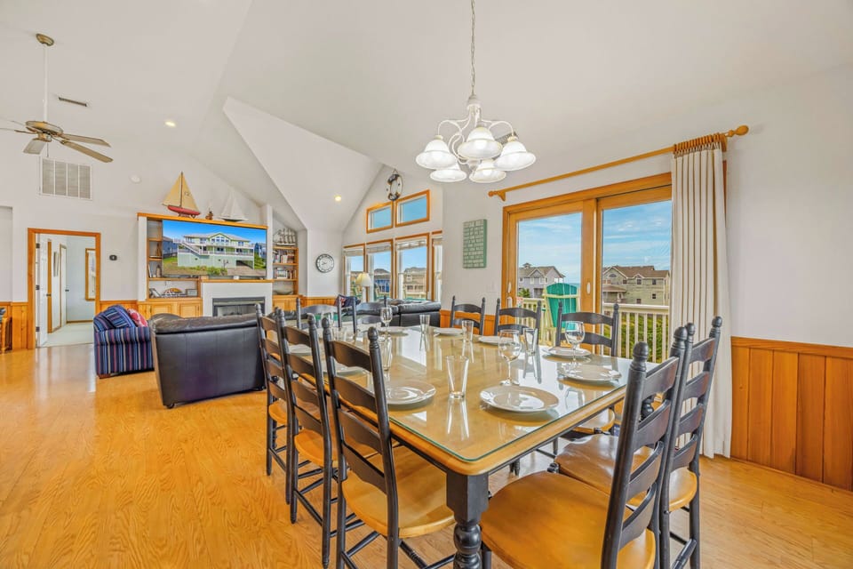 Open-concept living and dining area featuring vaulted ceilings, warm wood accents, and panoramic windows showcasing neighborhood views. Perfect for family meals and gatherings.