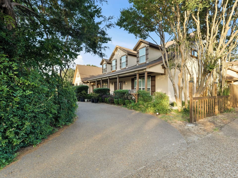 A spacious two-story vacation rental with attractive exterior architecture, nestled along a tree-lined driveway with mature landscaping and convenient parking access.
