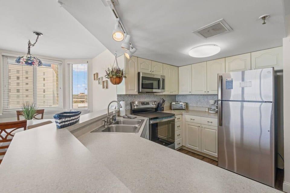 Fully equipped kitchen at The Pinnacle North Myrtle Beach Unit 506 includes major appliances, stainless steel dishwasher, microwave, fridge, freezer, stove, oven, bar seating, cookware, dishware, and silverware.