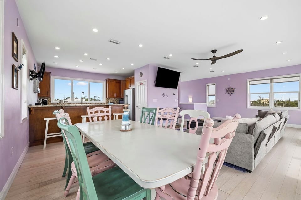 Gather around this inviting dining table, where mismatched pastel chairs add charm and personality. Beyond, your fully-equipped kitchen and cozy living area create a perfect open layout for relaxing or entertaining together.