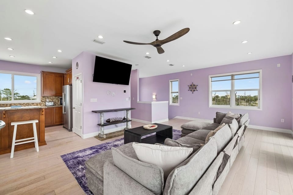 Sink into plush seating and enjoy movie nights in this bright, open living area with modern ceiling fan and large windows framing natural light.
