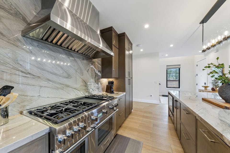 This chef's kitchen features sleek marble countertops, a professional-grade gas range, and modern wood cabinetry—ready for you to create culinary masterpieces or morning coffee in style.