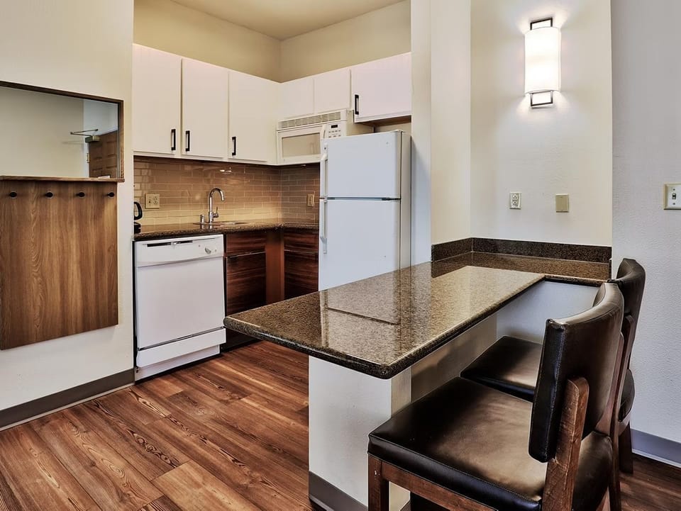Bright kitchen with sleek countertops, full stove, microwave, dishwasher, refrigerator, and a dining bar that seats 2