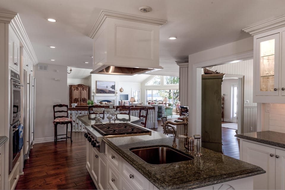 Dark granite countertop island with built-in stove and brass faucet overlooks hardwood floors and bright living space.