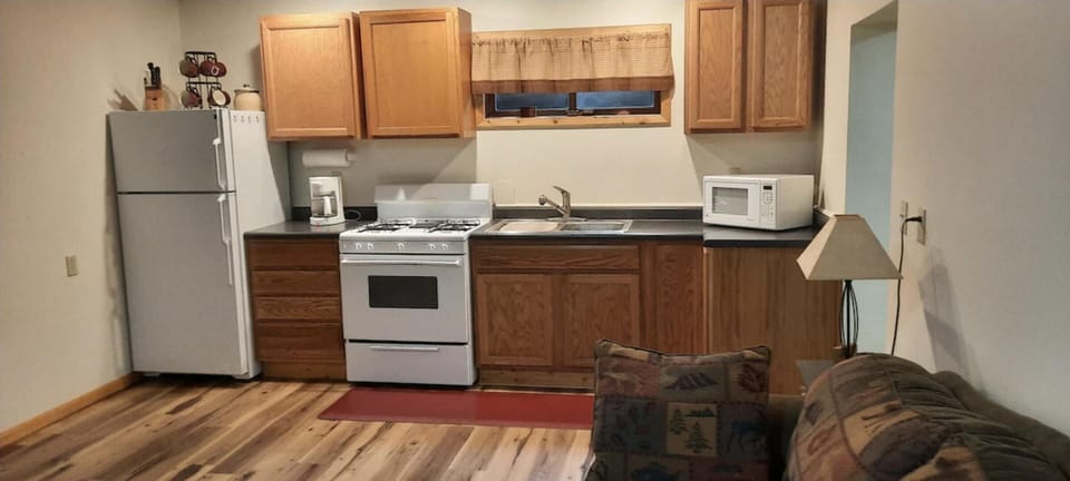 Compact kitchen with oak cabinets, white appliances, a single basin sink, and a patterned fabric couch nearby.