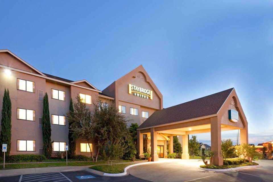 Hotel exterior at dusk with lit entrance, branded signage, and parking area.