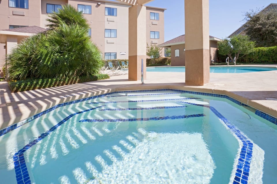 Hot tub with mosaic tile surround and outdoor pool with lounge chairs in the background.