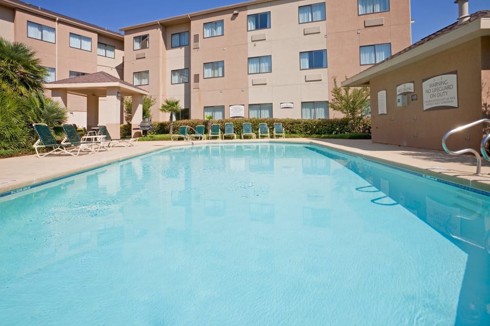 Outdoor pool with lounge chairs, shaded BBQ area, and the hotel building in the background.