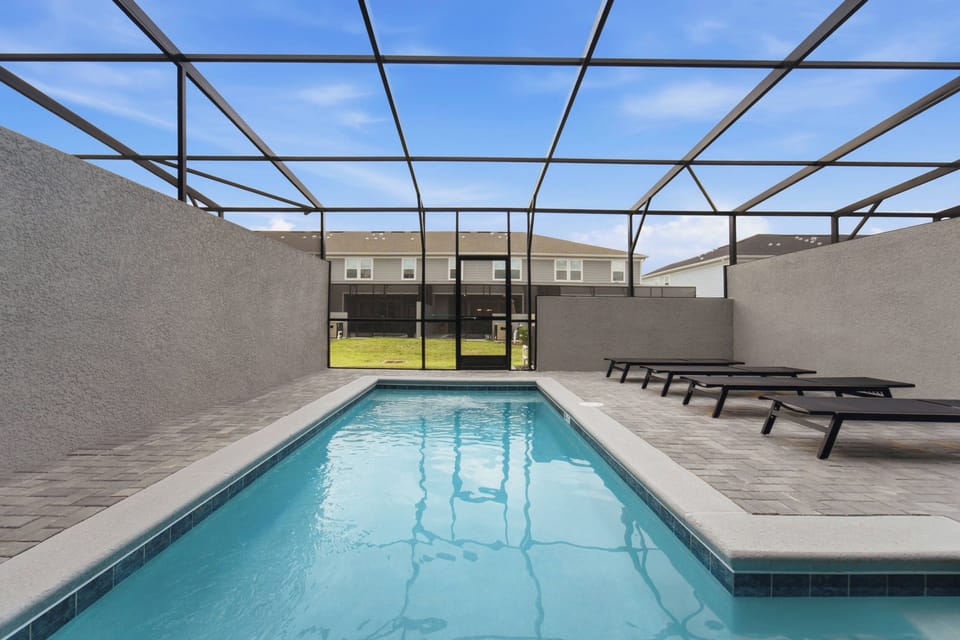 Relax in a private screened pool area with clear blue water, lounge chairs, paved deck, privacy walls, and open sky views, creating a refreshing space for family vacation moments.