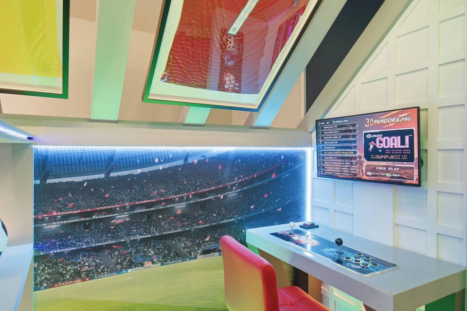Enjoy a soccer themed gaming nook with framed jerseys, stadium wall art, arcade controls, LED lighting, and a bright red seat, creating a fun space for vacation entertainment.