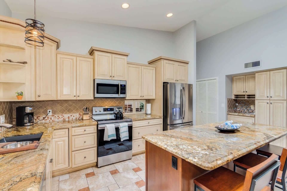 Open concept kitchen with stainless steel appliances, granite countertops, kitchen island with breakfast bar seating for 3, and coffee maker 