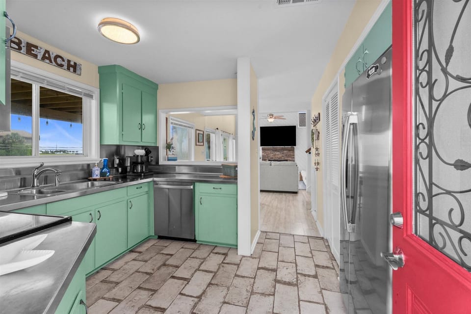 Coastal-style kitchen featuring stainless steel refrigerator, dishwasher, ample cabinetry, and an open layout connecting to the main living areas.