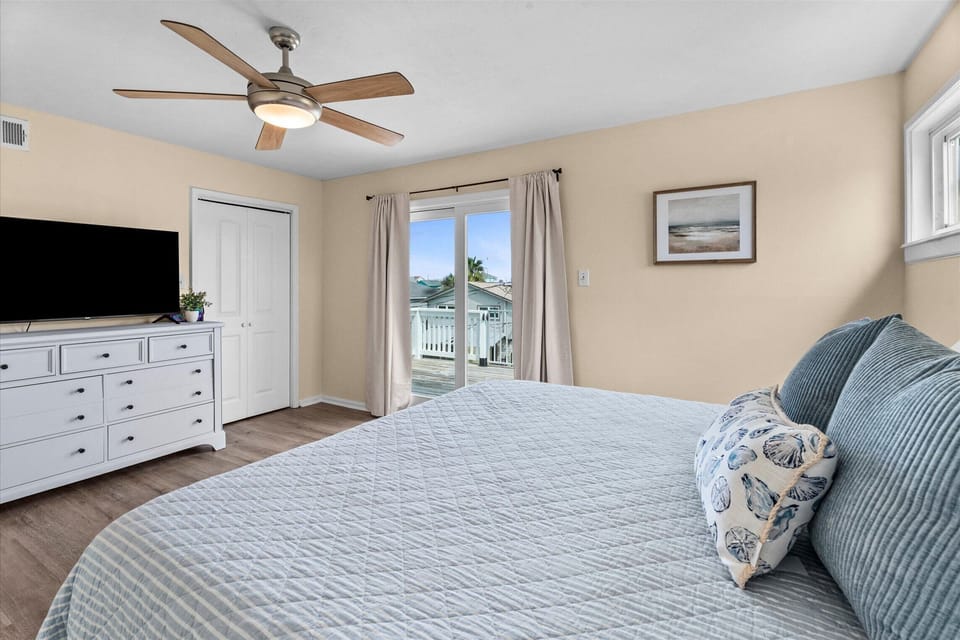 Well-appointed King bedroom featuring deck access, TV, dresser storage, and bright natural lighting throughout the space.