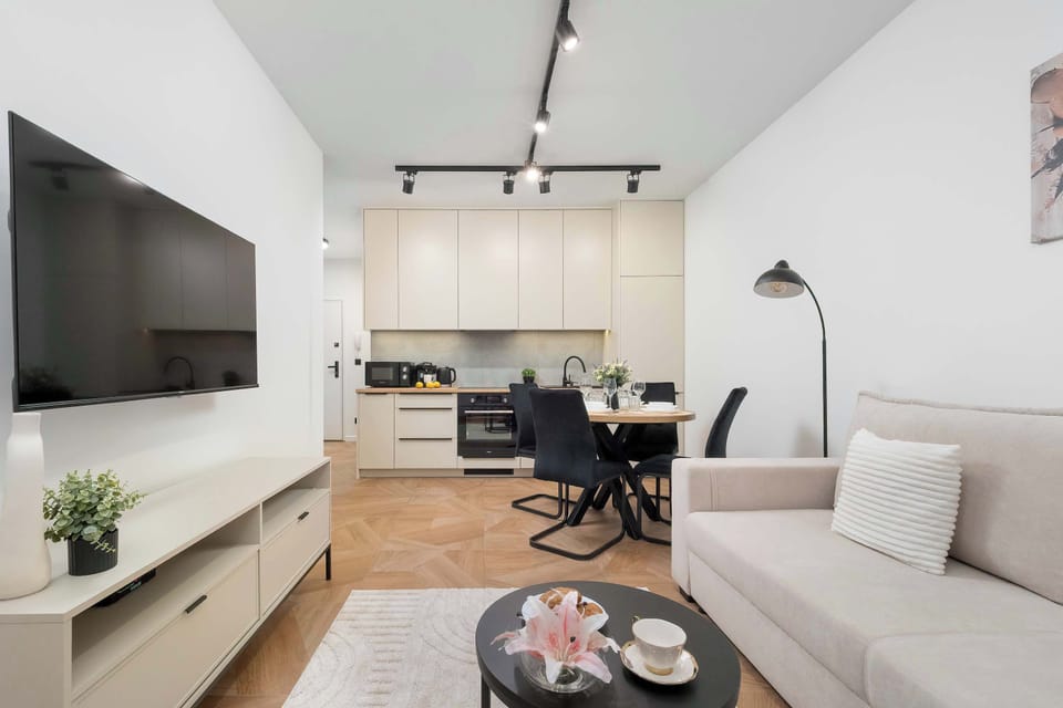A wide-angle view captures the open-concept living space, seamlessly connecting the living room sofa to the dining table and the kitchen in the background. Modern track lighting illuminates the entire area from the ceiling.