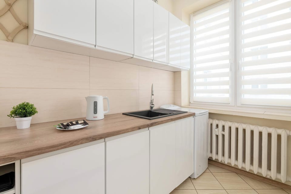 A bright kitchen with modern white cabinets and wooden countertops. Large windows make the space feel airy and welcoming.