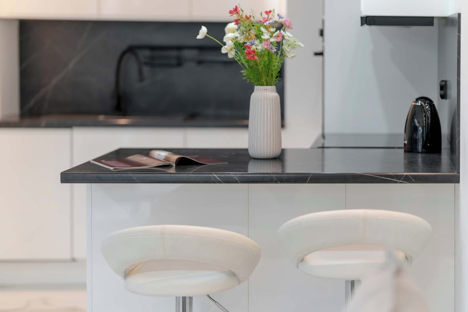 A functional kitchen island with a glossy black countertop serves as a breakfast bar, accompanied by two sleek white bar stools.