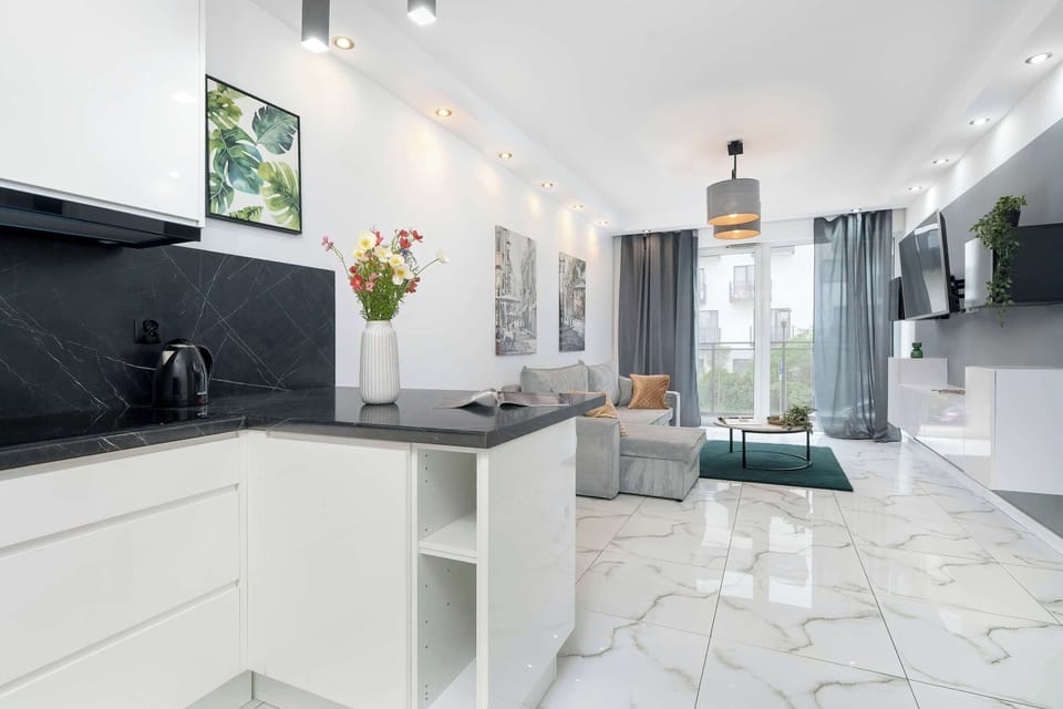 A bright, panoramic view captures the entire space: the fully equipped kitchen area, living space  and the sunlit windows at the far end.