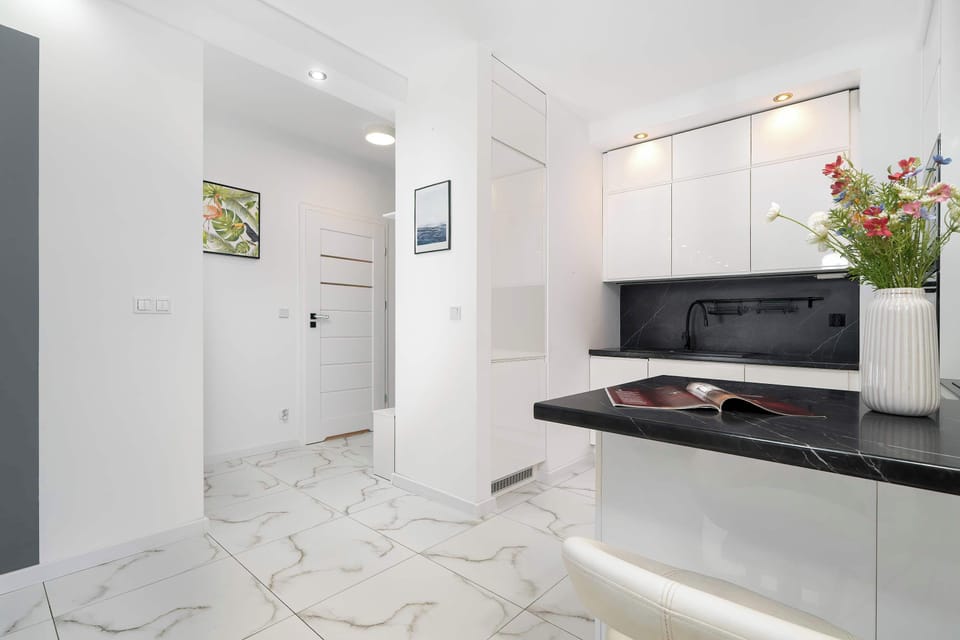 A compact entryway displays a pristine white hallway that opens up directly into a bright kitchen and dining zone.