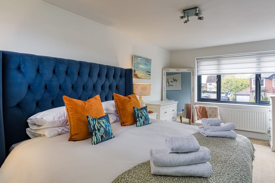 A bright welcoming bedroom featuring a statement upholstered bed, soft linens, and a peaceful, restful setting