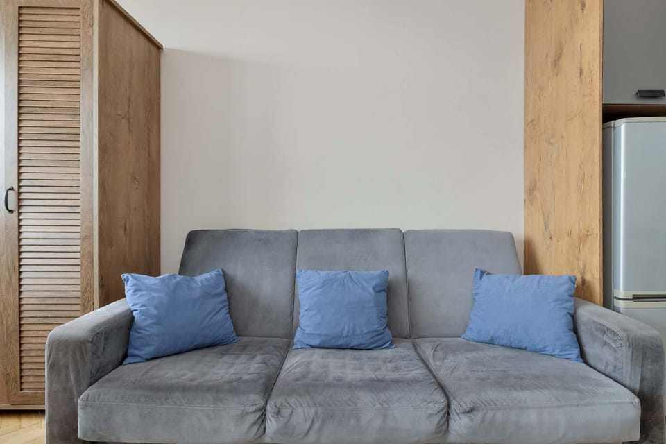 A close-up view focuses on a comfortable grey sofa adorned with three vibrant blue decorative pillows, positioned next to a rustic wooden wardrobe.