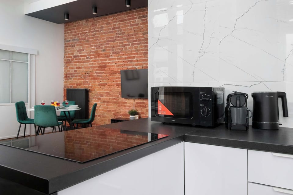 A compact kitchen view showing white storage units, a black countertop, and small kitchen appliances. The design is modern and uses a clean black-and-white color scheme.