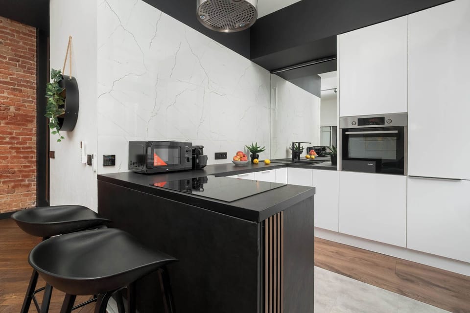 A sleek kitchen area with white cabinets, black countertops, and modern appliances. The space looks clean and organized with a simple contemporary style.