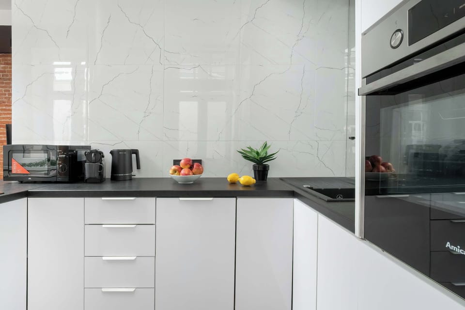 A white kitchen with built-in appliances, glossy cabinets, and a dark countertop. The room has a bright and practical layout for cooking and preparing meals.