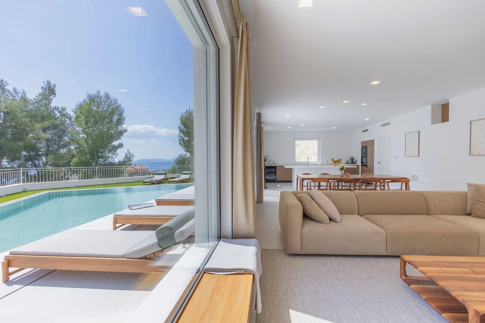 Bright open-plan living room with refined furniture from Prostoria and Artisan, large windows, and beautiful views of the sea and greenery