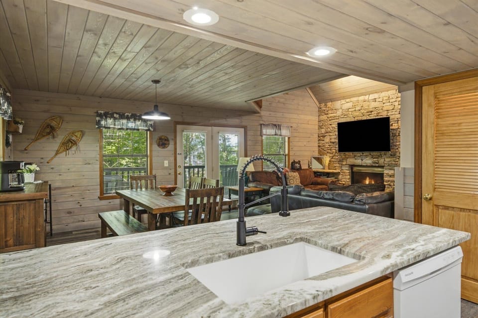 Your open-concept cabin retreat blends rustic charm with modern comforts—stone fireplace, sleek kitchen, and serene forest views from your private deck.