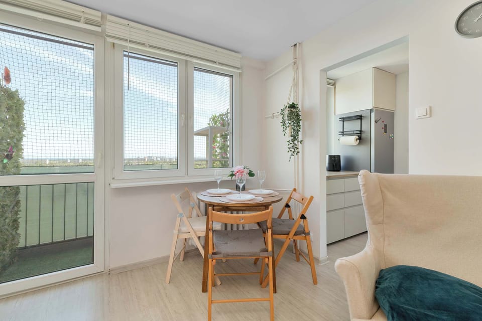 The dining corner features a circular wooden table paired with matching folding chairs, positioned right next to large windows that fill the dining area with natural daylight.