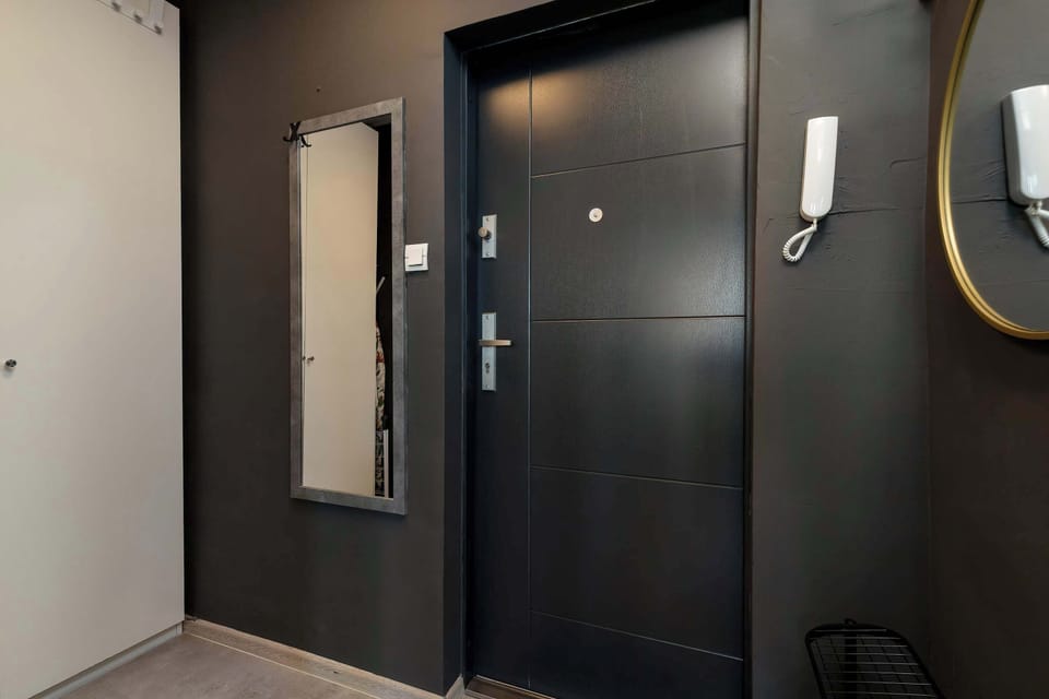 The entrance hallway features a dark, secure front door contrasted against a dark accent wall, complete with a wall-mounted mirror and an intercom system.