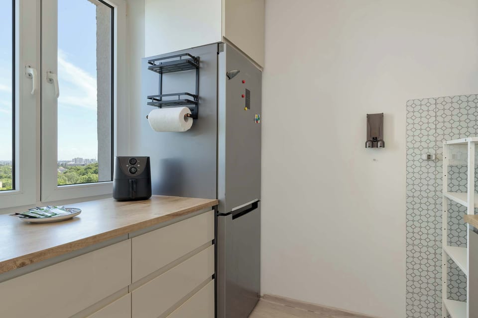 The kitchen area displays a tall stainless steel refrigerator standing next to a light wooden countertop with clean cabinetry beneath. A roll of paper towels is conveniently mounted on the tiled wall.