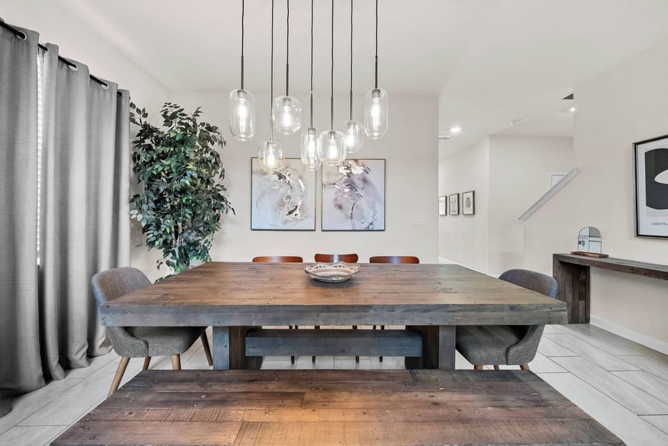 Savor unforgettable meals at our beautiful wooden dining table, where natural textures meet modern design beneath elegant pendant lighting, all in a warm atmosphere with cozy chairs and artistic wall decor.