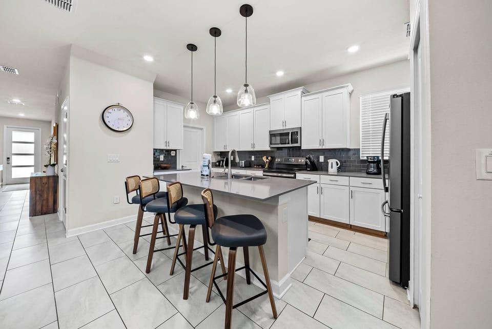 Welcome to this inviting kitchen featuring sleek white cabinets and modern stainless steel appliances. The spacious island and stylish bar stools create a perfect spot for casual gatherings, enhanced by warm pendant lighting and.