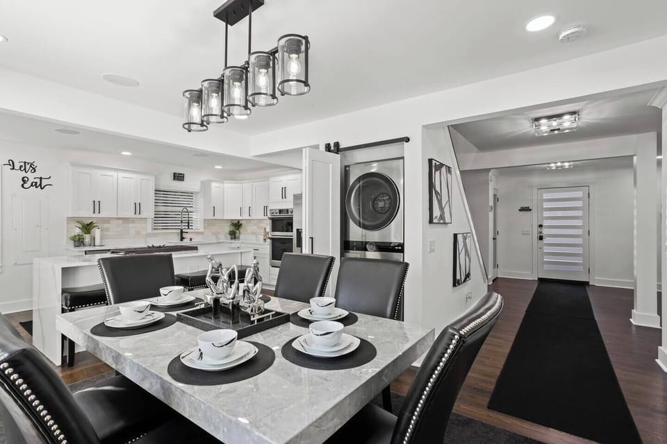 Modern dining space with a sleek marble-style table and seating for six. The adjacent kitchen offers a spacious quartz waterfall island and top-of-the-line appliances, including a stacked washer-dryer for convenience.