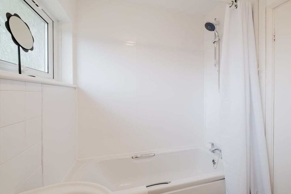 A bright and practical bathroom featuring a bath with an overhead shower for your convenience.