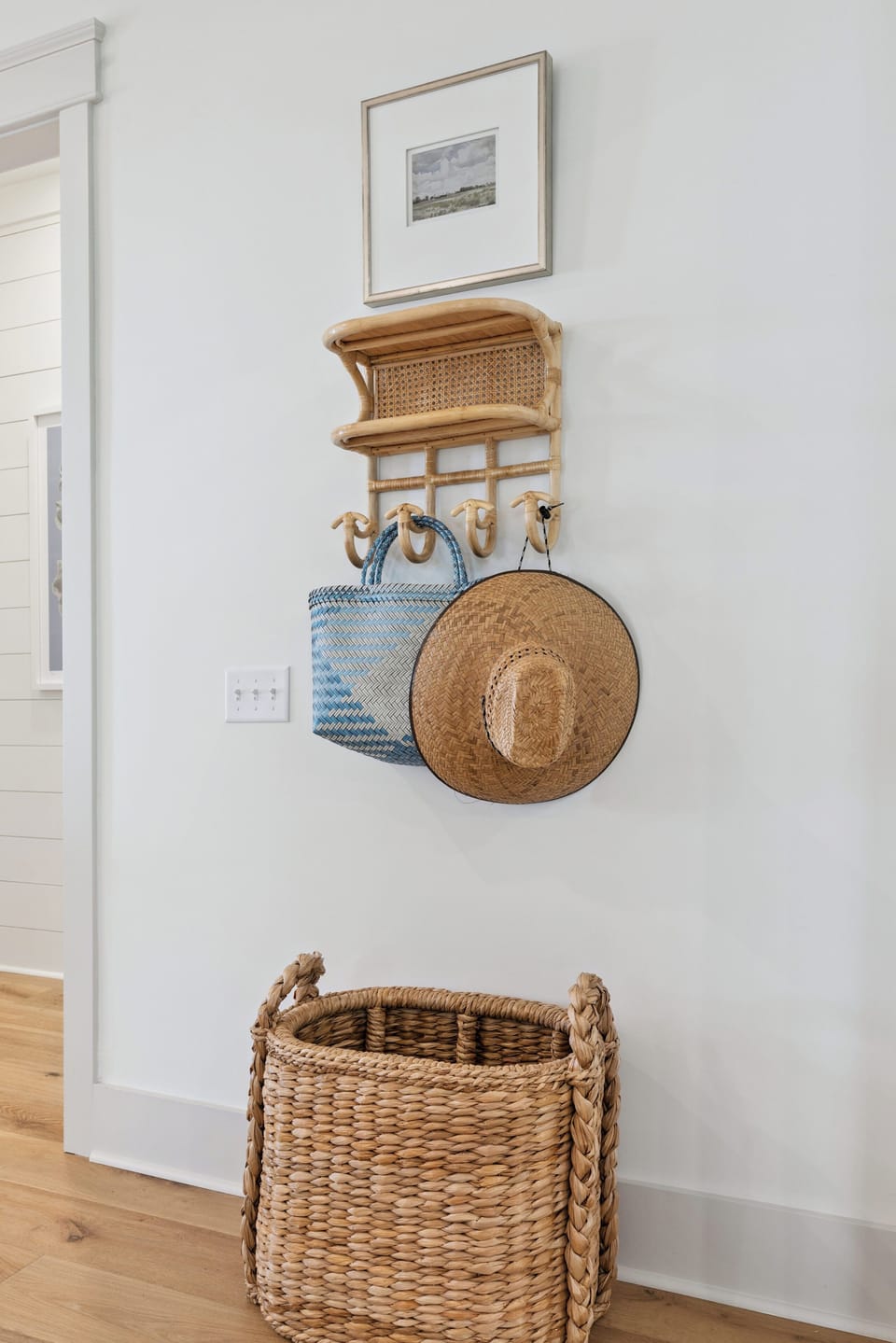 A thoughtful entryway corner with woven storage, wall hooks for your beach bag and sun hat, and a charming wicker basket—perfect for keeping your coastal essentials organized.