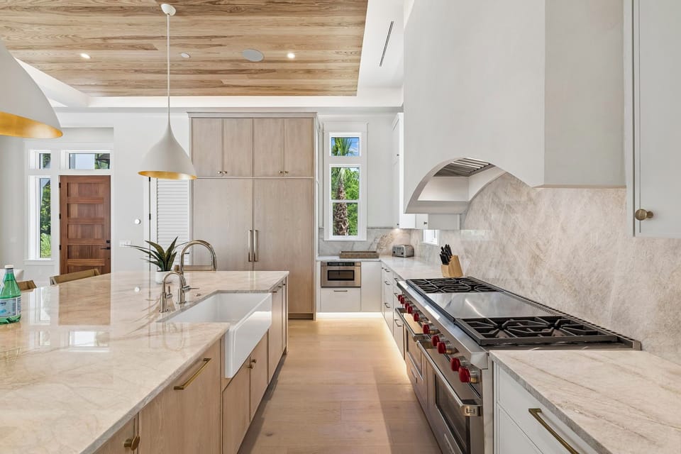 Your gourmet kitchen features stunning marble countertops, professional-grade appliances with bold red accents, and warm wood-toned ceilings. Natural light pours in, inviting you to create delicious meals in this elegant space.