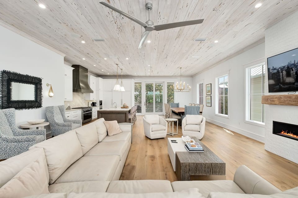 Unwind in your bright, open-concept living space featuring soaring whitewashed ceilings, plush seating, a cozy fireplace, and a fully equipped kitchen—perfect for relaxing evenings after exploring.