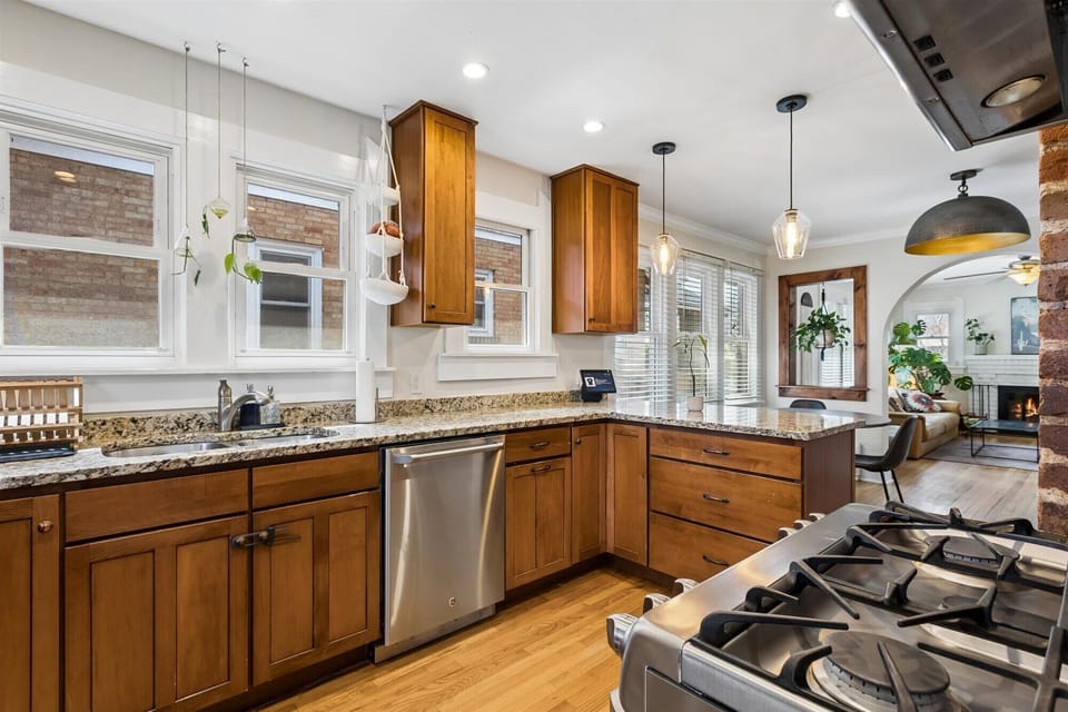 Bright, open-concept kitchen with a spacious granite breakfast bar, pendant lighting, and a clear view into a cozy living area with a fireplace.