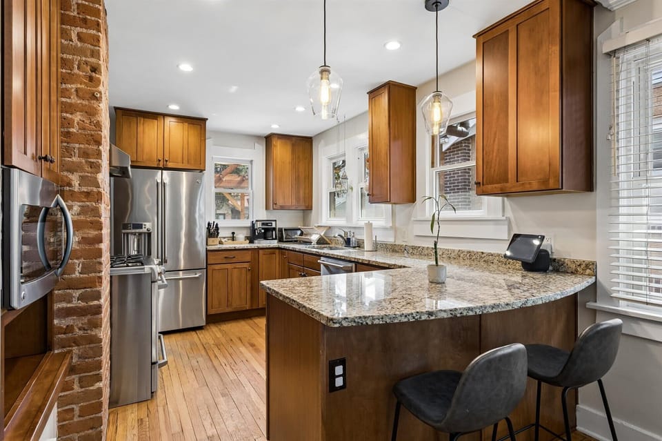 Updated Gourmet Kitchen with Exposed Brick Accent Modern kitchen featuring granite countertops, stainless steel appliances, warm wood cabinetry, and a charming exposed brick pillar for a loft-style feel.