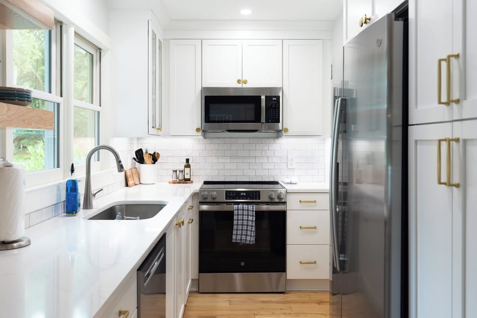A detailed view of the remodeled kitchen shows off the elegant subway tile backsplash, modern cabinetry with gold hardware, and a fully stocked setup complete with a stove, oven, microwave, and dishwasher.