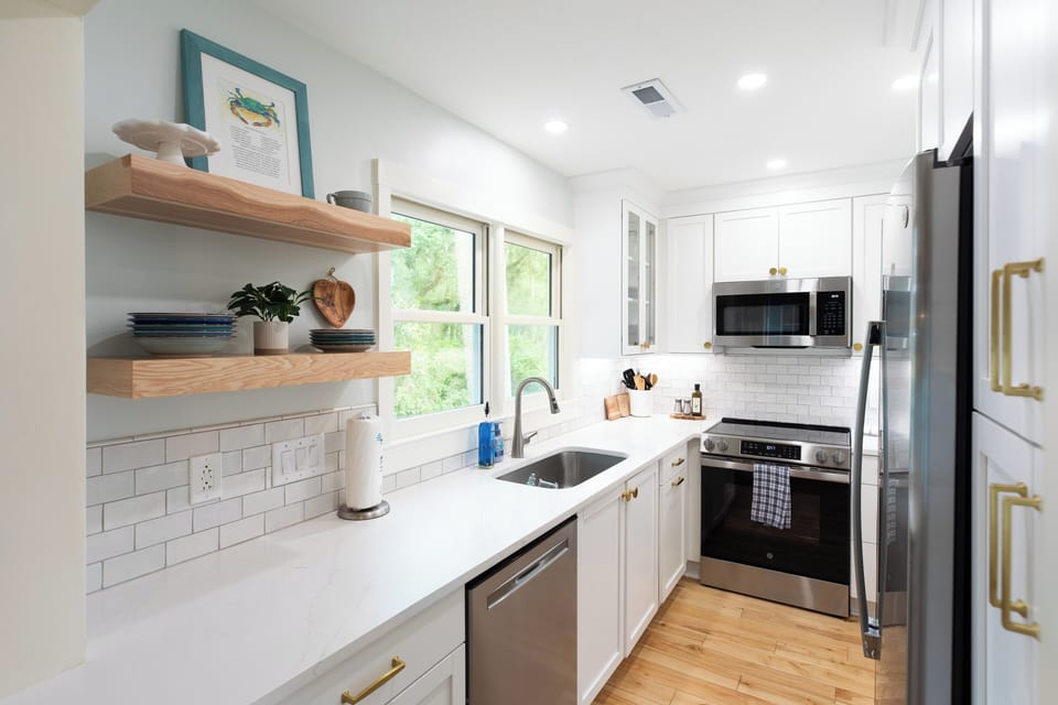 Another wide angle of the beautifully renovated galley kitchen showcases the seamless flow, under-cabinet lighting, and clean lines from the cooking range down to the deep stainless-steel sink.